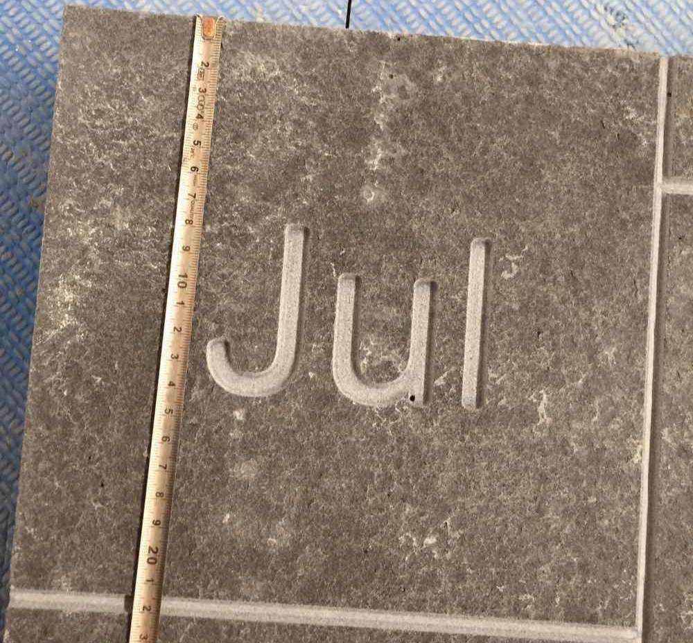 Flamed Mongolia Black basalt paver engraved with JUL, checked against a tape measure