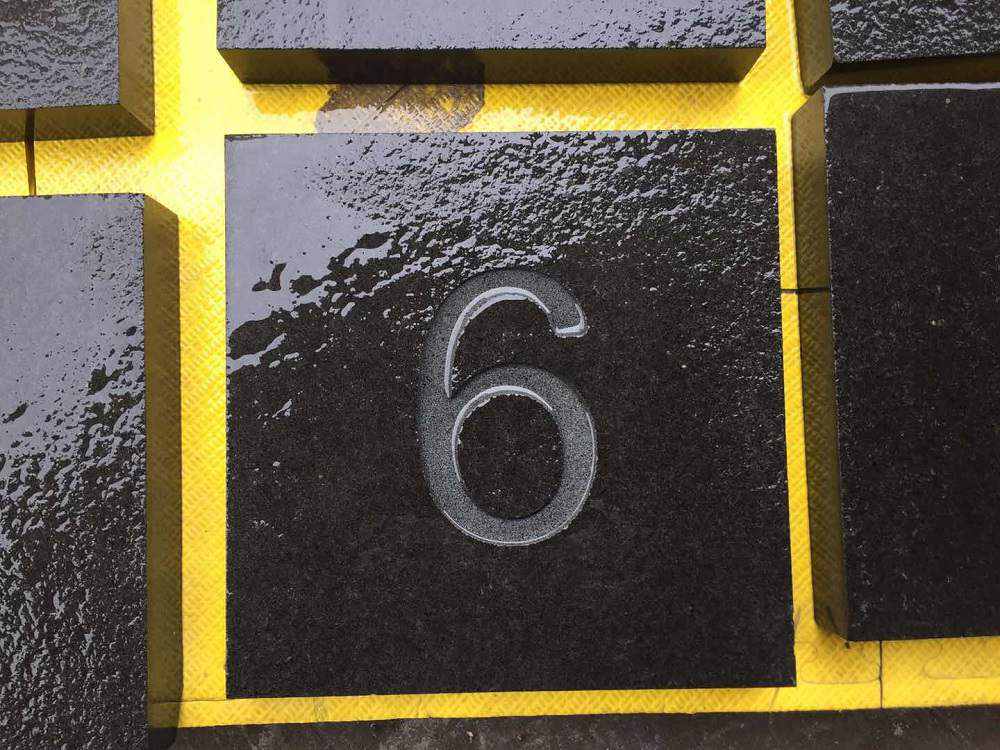Close-up of a polished black basalt tile with an engraved number six