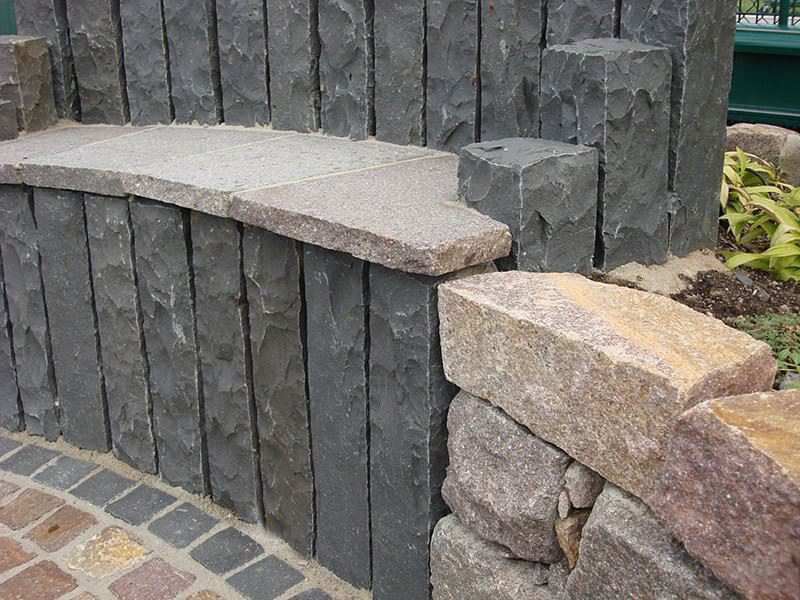 Curved retaining wall of basalt palisades with a stone coping