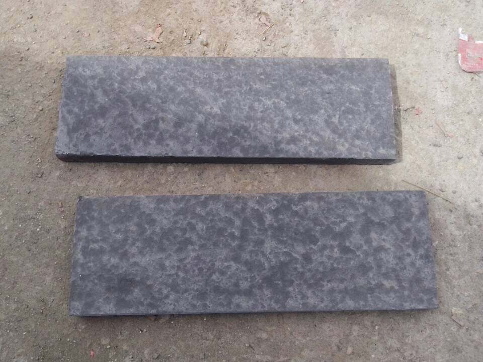 Two waterjet-finished Nergo Black basalt paving tiles with a softly textured surface
