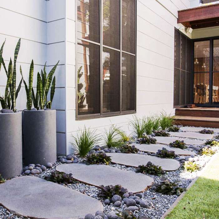 Rounded grey basalt stepping stones with planters beside a modern home